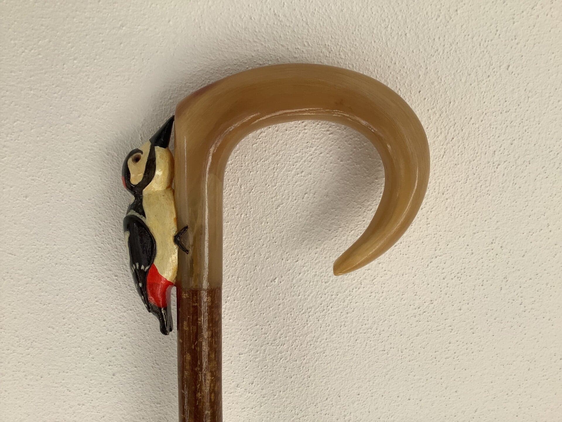 A horn crook handle with a carved and painted great spotted woodpecker